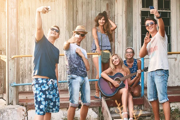 Junge Leute machen Selfie mit ihren Smartphones, während sie mit Freunden in der sommerlichen Holzhütte abhängen — Stockfoto
