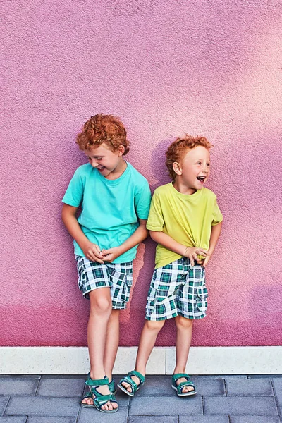 Dois bonitos meninos encaracolados vermelhos irmãos estão se divertindo rindo no fundo da parede rosa — Fotografia de Stock