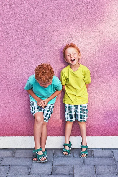 Dois bonitos meninos encaracolados vermelhos irmãos estão se divertindo rindo no fundo da parede rosa — Fotografia de Stock