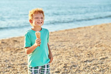 Şirin kırmızı kıvırcık çocuk, yaz kumsalında kirlenip dondurma yerken son derece mutlu.