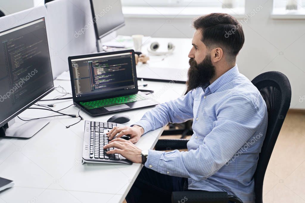 Computer programmer developer working in IT office, sitting at desk and coding, working on a project in software development company or startup.