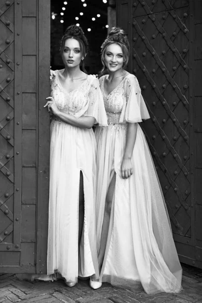 Όμορφα ρετρό στυλ παράνυμφοι κυρίες σε πανέμορφο κομψό κομψό φως γκρι ασημί φορέματα μήκος δαπέδου στην παλιά όμορφη ευρωπαϊκή πόλη καλωσορίζουν τους επισκέπτες στην πύλη. Μαύρο και άσπρο. — Φωτογραφία Αρχείου