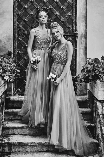 Beautiful bridesmaids in gorgeous elegant stylish floor length v neck chiffon gown dress decorated with sequins sparkles and rhinestones holding flowers bouquets. Wedding day in old beautiful European — Stock Photo, Image
