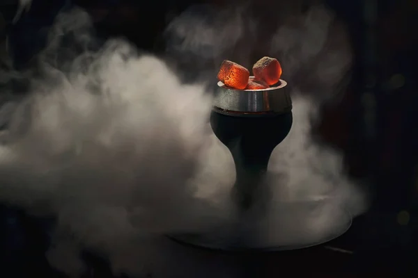 Siyah arka planda güzel beyaz duman bulutları içinde kırmızı kömürlü son moda nargile kasesi. Rahatlamak ve sigara içmek için hindistan cevizi kömürü ile modern shisha.