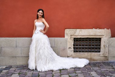 Güzel gelin, zarif, beyaz bir zemin üzerinde eski güzel Avrupa şehrinde düğün günü giydiği elbiseyle..