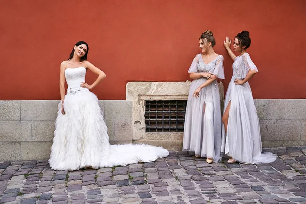 Schöne Braut und Brautjungfern in wunderschönen eleganten eleganten hellgrauen bodenlangen Kleidern in alten schönen europäischen Stadt Spaß an einem Hochzeitstag. — Stockfoto