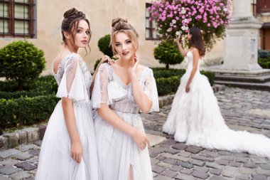 Güzel gelin ve nedimeler zarif, şık, açık gri gri zemin uzunluğunda bir düğün gününde eski güzel Avrupa şehrinde giyinirler..