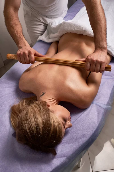 Masseur masculin faisant massage japonais avec des bâtons de bambou sur beau corps de femme nue dans le salon de spa. Concept de traitement beauté . — Photo