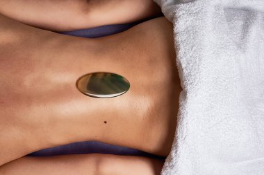 Geleneksel Çin nefrit oval gua sha masaj aletini kaplıca salonundaki yağlı, çıplak kadının arkasına sürterek. Güzellik tedavi konsepti.