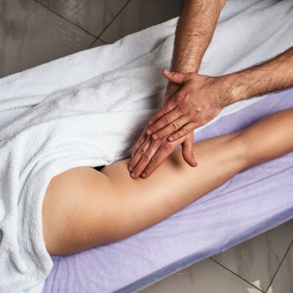 Masażysta robi masaż na udzie pięknej nagiej kobiety w salonie spa. Koncepcja pielęgnacji. — Zdjęcie stockowe