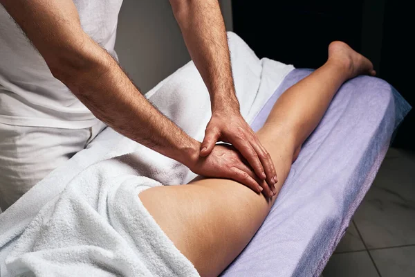 Masażysta robi masaż na udzie pięknej nagiej kobiety w salonie spa. Koncepcja pielęgnacji. — Zdjęcie stockowe