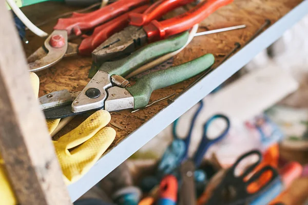 Old instruments such as wire cutters, diagonal pliers, garden scissorson and working gloves on a shelf in garage — Stock Photo, Image