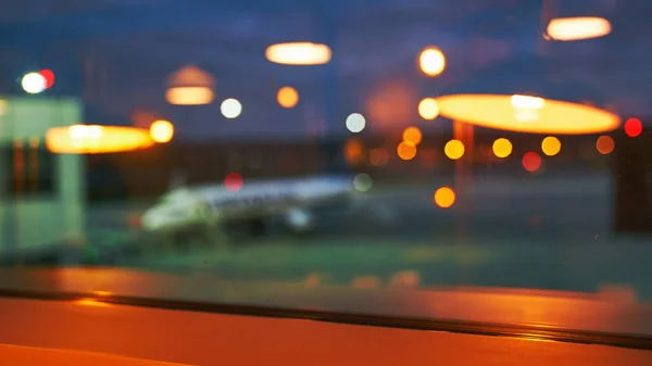 Blurred or defocused beautiful airport terminal early morning or night background with airplane, bokeh lights and glass reflections