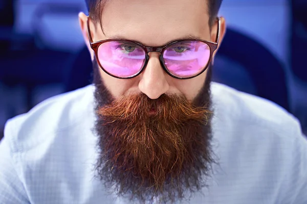 Бородатий чоловік в окулярах з відображенням екрану, що працює на комп'ютері в ІТ-офісі, сидить за кодом письма, працює над проектом в компанії з розробки програмного забезпечення або стартапу . — стокове фото