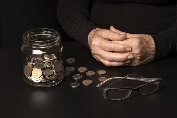 The concept of pension reform. Against the dark background of the hands of an old woman and jar of coins