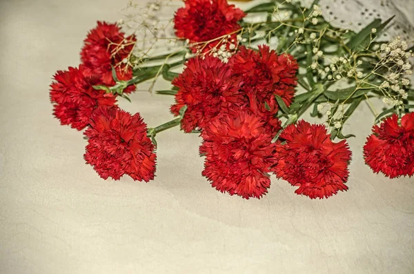 Große rote Nelken mit weißen getrockneten kleinen Blumen auf dem Tisch bedeckt ein zartes Tuch — Stockfoto