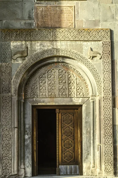Holztür, bedeckt mit einem geschnitzten ethnischen Ornament, und ein steinernes ovales Flugzeug mit geschnitzten Fruchtmustern über der Eingangskirche von Katoghike im Geghard-Kloster. — Stockfoto