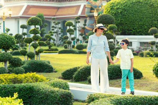 Ung mor og hendes lille søn går i grønne bonsai træer haver i Wat Arun - Stock-foto