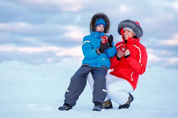 Schattige kleine jongen en zijn moeder drinken van hete thee op ijzige strand — Stockfoto