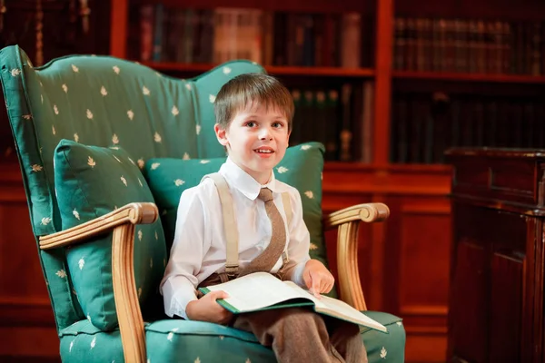 Cute little boy reading book on armchair — Stock Photo, Image