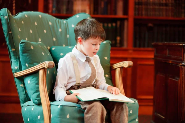 Netter kleiner Junge liest Buch auf Sessel — Stockfoto