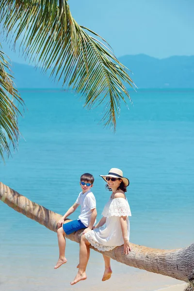 Moeder en zoontje op tropisch strand zittend op palmboom — Stockfoto