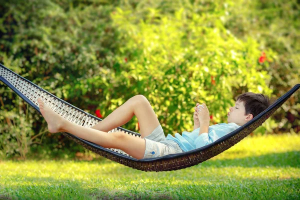 Side view of cute little boy lying on a hammock looking at his cell phone — Stock Photo, Image