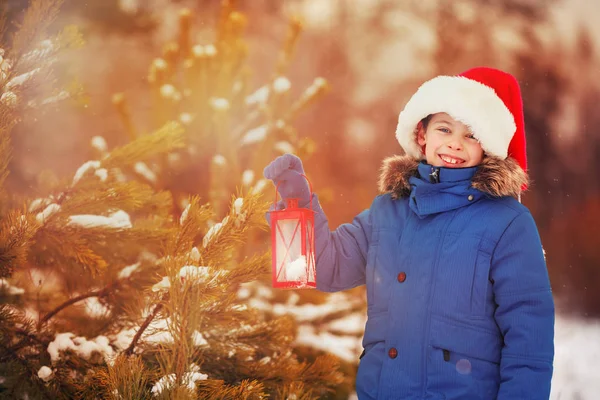 Menino bonito segurando lanterna de Natal ao ar livre no dia de neve de inverno — Fotografia de Stock