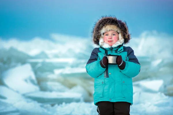 Söt fem år gammal pojke dricker varmt te på vintern fryst havet — Stockfoto