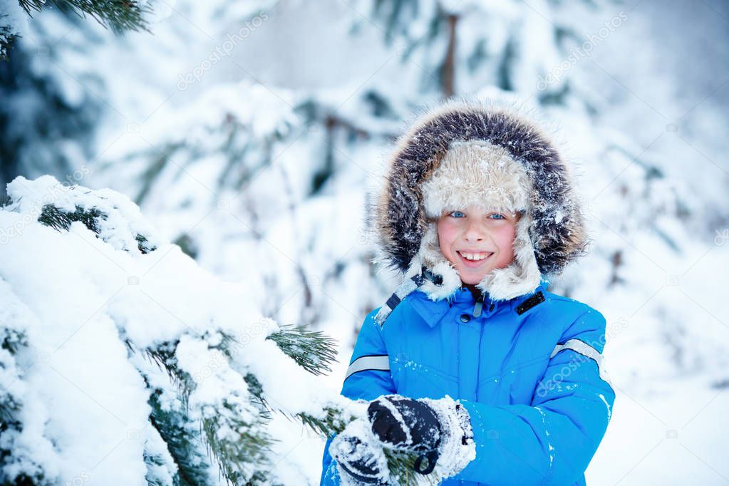 Cute little boy wearing warm clothes playing on winter forest