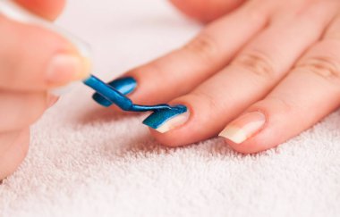 Orta parmak üzerinde koyu mavi parlak tırnak cilası uygulayarak kadın