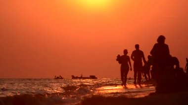 Akşam yürüyüş kıyı boyunca. Gün batımında siluetleri. Bir grup insan. Akşam sahilde yürümek. Günbatımında bir yürüyüş. Yaz sahil. Islak kum üzerinde yürüme.
