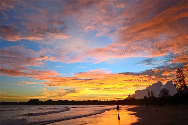 Apus de soare la tropice pe coasta oceanului. Silueta unei fete care merge pe plajă. Culorile luminoase ale cerului se reflectă în apă și nisip . — Fotografie, imagine de stoc