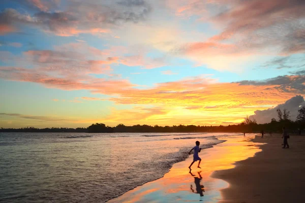 Apus tropical pe coasta oceanului. Copilul sare pe plajă. Culorile luminoase ale cerului se reflectă în apă și nisip. Sri Lanka — Fotografie, imagine de stoc