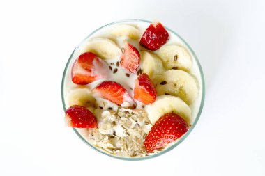 Kahvaltı - yulaf gevreği çilek ve muz ve beyaz bir arka plan üzerinde bir cam kabı içinde keten tohumu ile beyaz ev yapımı yoğurt detoks. Üstten Görünüm