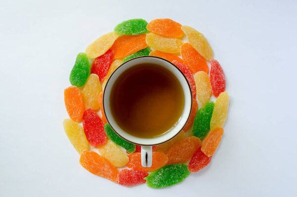 A cup of tea and colored pineapple candied fruits in a circle. 