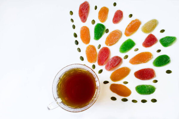 Sweets and black tea in glass cup with colorful pineapple candies and pumpkin seeds on a white background. Copy space