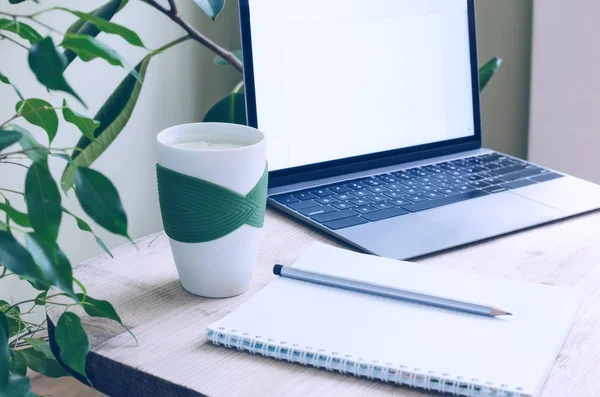 Un moderno ufficio posto di lavoro circondato da piante verdi. Un tavolo di legno con un computer portatile, notebook, matita e una tazza di acqua e limone. Immagine tonica — Foto Stock