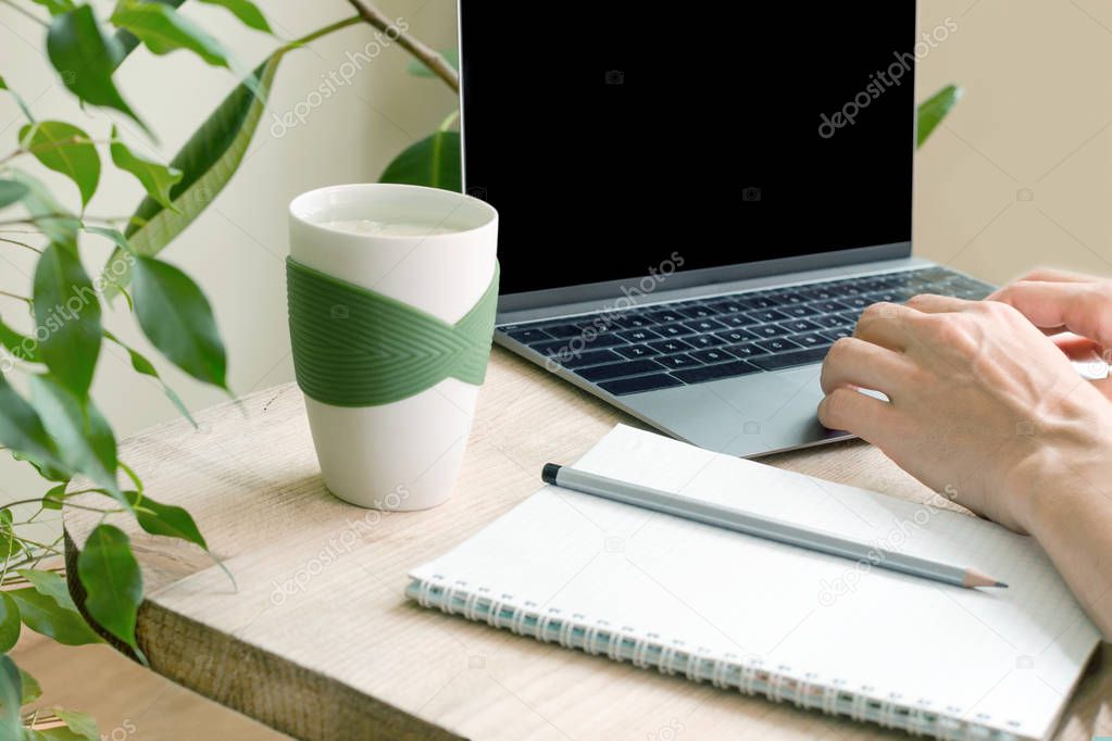 Hands of a woman who works for a laptop. A workplace in an apartment amongst green plants