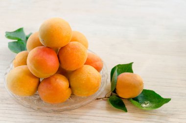 Kayısı ile su damlaları ve dalları üzerinde yeşil yaprakları ile güneş ışınları tarafından yaktı bir cam daire üzerine dizilir. Taze olgun kayısı. Ahşap arka plan.