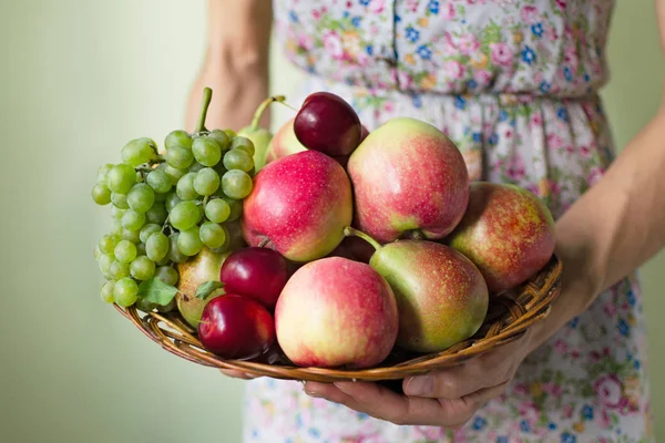 Женские руки держат плетеную деревянную тарелку с жатвой осенних фруктов. Концепция сбора урожая — стоковое фото