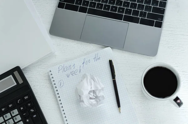 Escritório de negócios local de trabalho com laptop, calculadora, xícara de café. Um plano de trabalho para uma semana é elaborado no bloco de notas. Vista superior — Fotografia de Stock