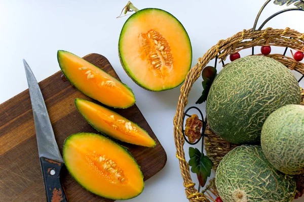 Olgun kavun, yeşil bir kabuk ile sarı içinde tüm ve kesilmiş bir sepet içinde ve bir masada yalan.