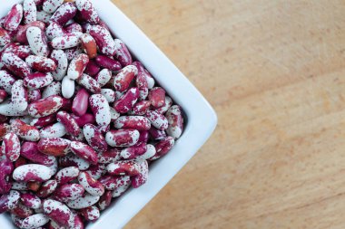 Fasulye çeşitleri Swallow kırmızı ve beyaz noktalı ahşap arka plan üzerinde beyaz bir seramik kase. Üstten Görünüm.