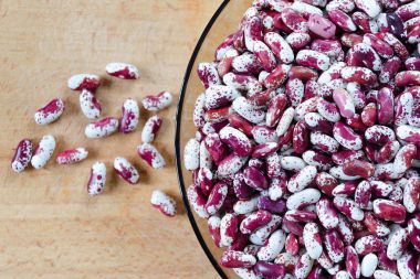 Barbunya fasulyesi mor, kırmızı ve beyaz renkleri nokta, Swallow çeşitleri bir cam ile ahşap bir arka plan üzerinde plakası. Üstten Görünüm.