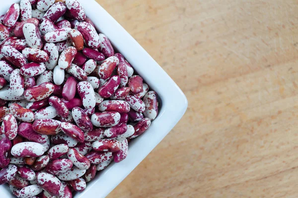 Fasulye çeşitleri Swallow kırmızı ve beyaz noktalı ahşap arka plan üzerinde beyaz bir seramik kase. Üstten Görünüm.