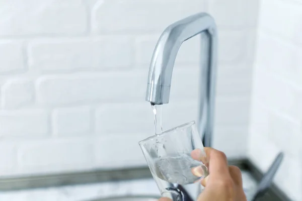 Hand houdt het glas, vullen met water uit de kraan. — Stockfoto