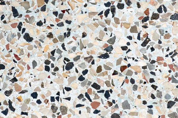 Multi-colored small flat stones are immersed in concrete. Abstract background.