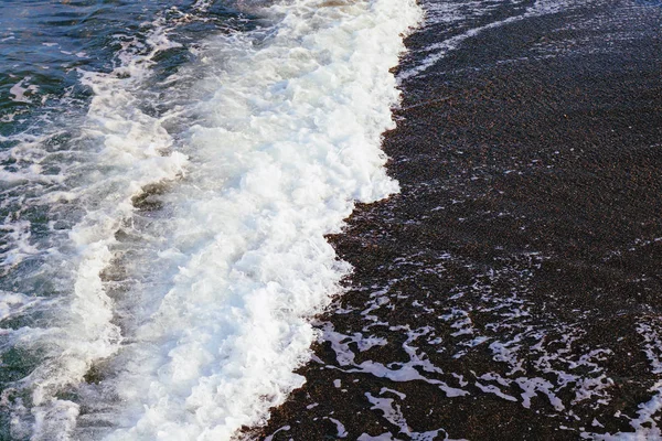 Морская волна с белой пеной на темном песке . — стоковое фото