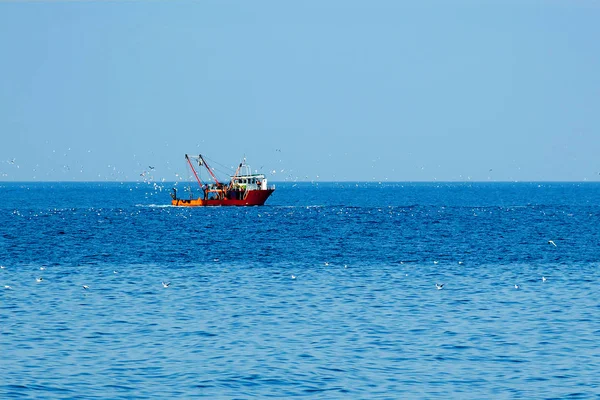 A red fishing ship in the open sea surrounded by birds. Minimalistic landscape. — Stock Photo, Image